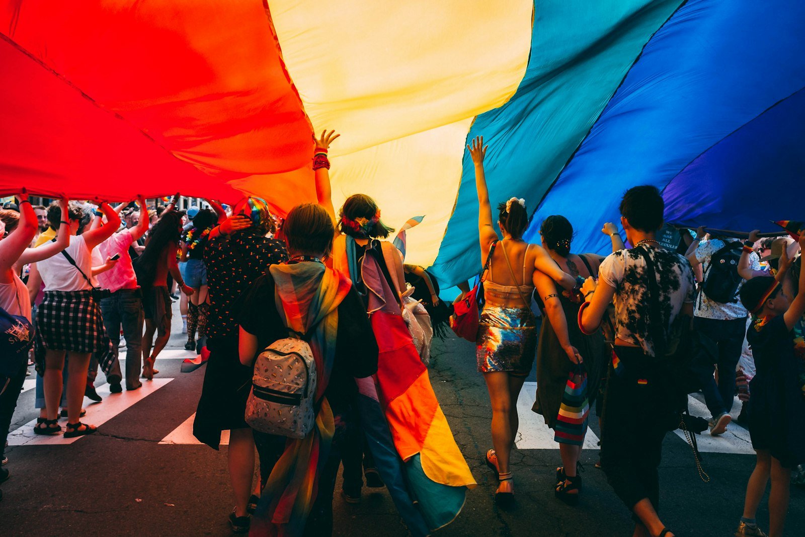 Personas caminando bajo una gran bandera arcoíris en una calle de la ciudad